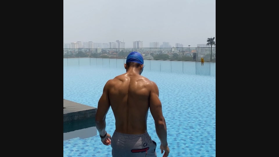 An athlete faces an outdoor pool and distant skyline in daylight.
