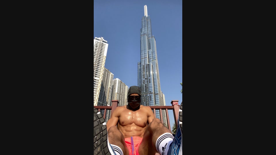 A masked athlete seated after outdoor training, photographed from a low angle against a high-rise skyline.