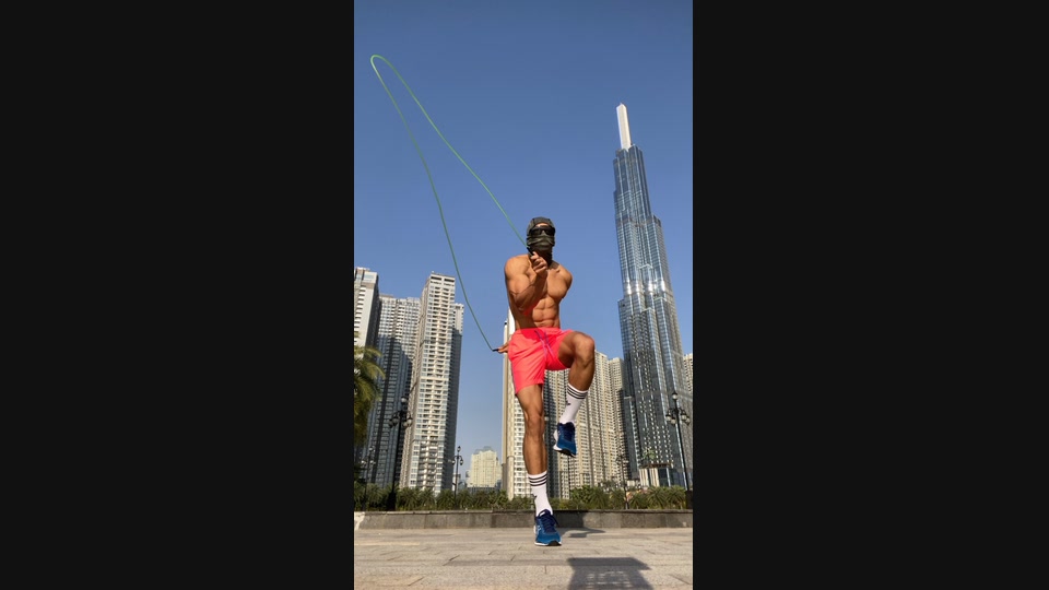 A masked athlete performs a jump-rope movement in an outdoor urban setting.